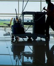 Person mit Reinigungswagen auf einem Flughafen. draußen ist eine Landebahn zu sehen.