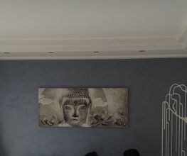 Parete soggiorno grigia con dipinto di Buddha, decorazioni floreali viola e luce soffusa.