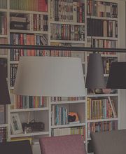 Bücherregal mit Lampen im Vordergrund; bunte Buchrücken und moderne Esszimmerstühle sichtbar.