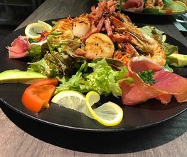 Ein Teller mit Meeresfrüchtesalat, Avocado, Tomaten, Salat und Zitronenscheiben.