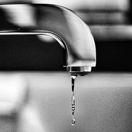 Close-up of a faucet dripping water, captured in black and white.