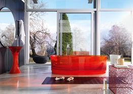 Bagno moderno con vasca rossa trasparente, vista su giardino e montagna attraverso ampie vetrate.
