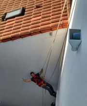 Un obrero colgado en unas cuerdas sonríe y toma una foto en una fachada blanca.