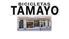 Tienda "Bicicletas Tamayo" con escaparate de bicicletas y logotipo grande sobre el techo.