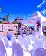 Ceremonia de boda al aire libre junto al mar con sillas blancas y una carpa decorada.