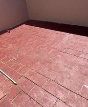 Baldosas rojas en una terraza con sombra parcial y una pared blanca al fondo.