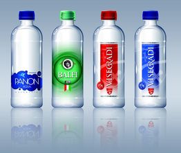 Cuatro botellas de agua en fila con etiquetas de diferentes colores sobre un fondo azul claro.