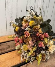 Ramo de flores secas con rosas pequeñas y hojas verdes sobre fondo de madera y pared blanca.