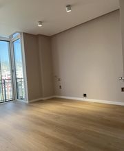 Sala vacía con piso de madera, ventana grande y paredes beige claro.