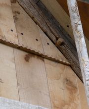 Holzwand mit sichtbarer Struktur und Nagelbefestigung, umrahmt von einem Metallgerüst.