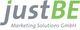 Logo von justBE Marketing Solutions GmbH mit grauem und grünem Text.