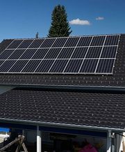 Dach mit Solarmodulen, blauer Himmel, Bäume im Hintergrund.