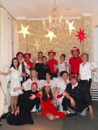 Gruppe von Menschen in rot-weißer Kleidung posiert lachend vor festlicher Dekoration.