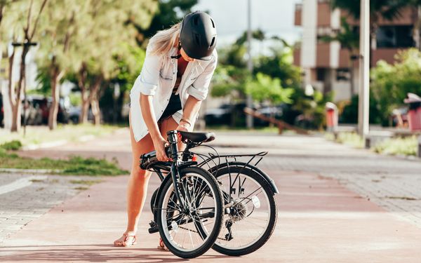 Frau mit Helm klappt Klapprad auf einem Gehweg auseinander.