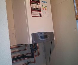 Calentador de agua montado en la pared con conexiones de tuberías visibles a la izquierda.