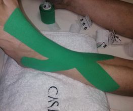 Vendaje kinesio verde en el pie y pierna sobre una toalla blanca.