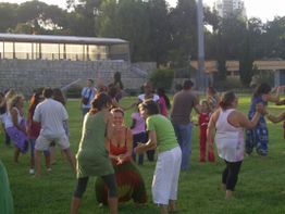 Gruppe von Menschen tanzt und spielt fröhlich im Park auf einer sonnigen Wiese.