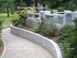 Steinpfad im Garten mit Brücke, Pflanzen und Kontaktdetails von Brunstorfer GaLaBau.