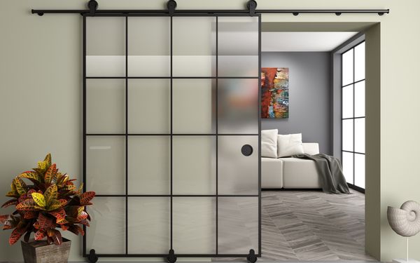 Glasschiebetür mit schwarzen Verstrebungen an einer beigen Wand. Die Tür führt in das dahinter gelegene Schlafzimmer.