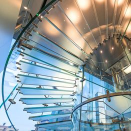 Spiral glass staircase with city views through floor-to-ceiling windows.