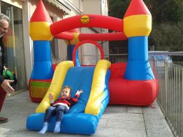 Kleinkind rutscht auf blauer Hüpfburg-Rutsche, daneben eine Person mit roter Hose.