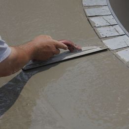 Hand smoothing wet cement with a trowel near a curved tiled edge.