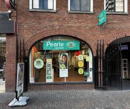 Gevel van een Pearle opticienwinkel in een bakstenen gebouw, met diverse posters en logo's.