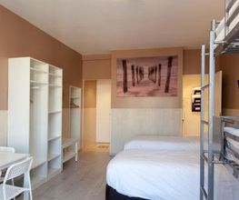 Helles Zimmer mit Etagenbett, Doppelbett, Tisch, Stühlen und Bild an der Wand.