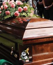 Bara di legno con fiori rosa, circondata da persone in abiti scuri in un ambiente all'aperto.