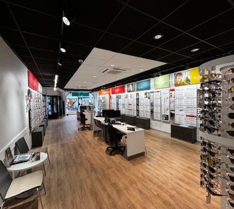 Optiekwinkel interieur met brillenrekken en tafels op houten vloer.