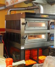 Ein Pizzabackofen in einer Küche mit Kacheln und Edelstahlgeräten im Hintergrund.