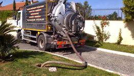 Camion autospurghi in azione, con tubo collegato a tombino in un vialetto residenziale.