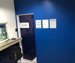 Parede azul com placa "SALA VIP", janela de atendimento e cadeira preta em um ambiente interno.