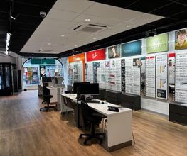 Optiekwinkel met brillen aan de muur, bureaus en stoelen op een houten vloer.