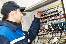Technician in blue uniform fixing an electrical panel with a screwdriver.