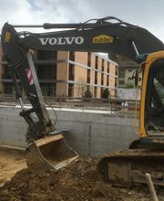 Bagger bei Bauarbeiten vor einem modernen Gebäude mit Ziegel- und Glasfassade.