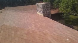 Roof with red shingles and a brick chimney, surrounded by green trees.