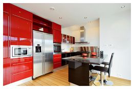 Moderne Küche mit roten Schränken, Edelstahlgeräten und einem schwarzen Esstisch mit Stühlen.