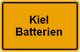 Straßenschild in Orange mit der Aufschrift "Kiel Batterien" in schwarzer Schrift.