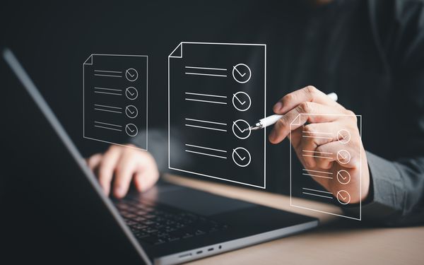 Mann hakt symbolisch eine Grafik in Form einer To Do Liste vor seinem Laptop ab.