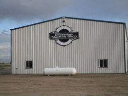 Metal building with "Crestview Machine Shop" sign and a white tank in front.