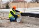 Worker applying sealant to a concrete foundation, wearing a safety vest and helmet.