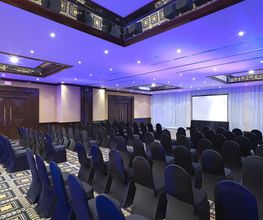 Sala de conferencias con sillas negras y proyector, iluminada con luz azul en el techo.