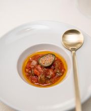 Plato elegante con salsa roja y una cucharilla dorada al lado, sobre un mantel blanco.