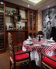 Mesa con mantel rojo y blanco en restaurante con mural de fotos antiguas y botellas de vino.