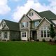 Two-story stone house with large windows and a green lawn under a partly cloudy sky.