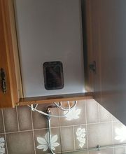 Calentador de agua blanco en un gabinete de cocina con recipiente azul debajo.