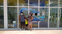 Persona con mascarilla frente a oficina de alquiler de autos "City Rent" con familia.