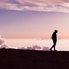 Eine Person spaziert bei Sonnenuntergang am Horizont entlang, der Himmel ist rosa und lila.