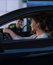 Conductora sonriente en una gasolinera, atendida por un empleado que se inclina hacia la ventana.